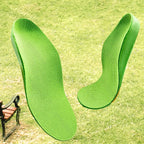 Par de palmilhas ortopédicas X infantis 3d verdes anatômicas ambientadas flutuando sobre fundo de grama e banco de madeira, destacando o suporte de arco médio Universo Vigor Saúde