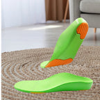 Par de palmilhas ortopédicas X infantis 3d, para pés chatos, planos, pisada pronada, verdes anatômicas ambientadas sobre tapete de corda em sala de estar, destacando o perfil de suporte e amortecedores Universo Vigor Saúde