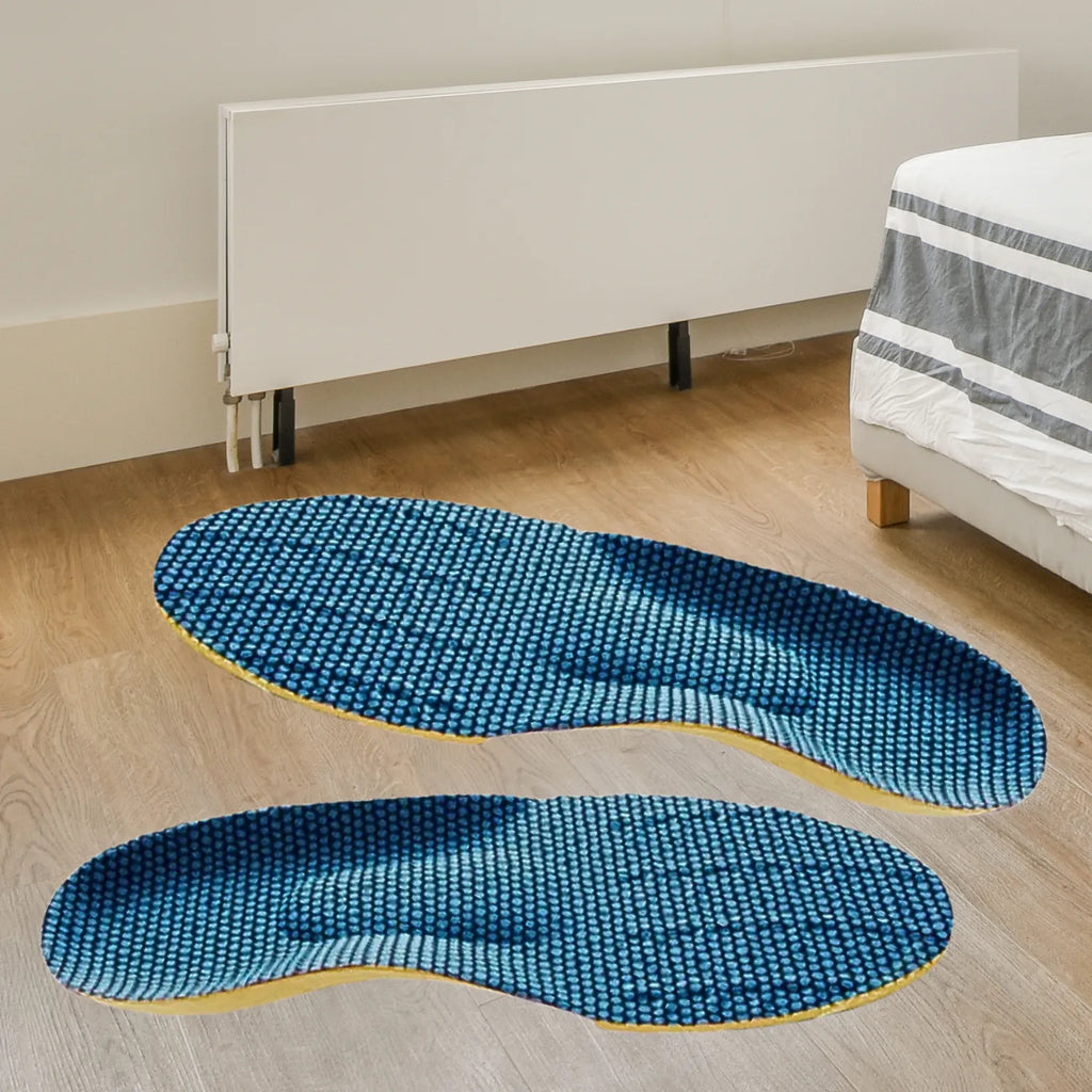 Par de palmilhas ortopédicas X ergonômicas, para pés chatos, planos, pisada pronada, de cor amarela disposto sobre piso de madeira clara em cenário de quarto com cama ao fundo, exibindo a superfície superior em tecido azul texturizado alveolar