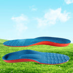 Par de palmilhas ortopédicas X, para pés chatos, planos, pisada pronada, com superfície superior em tecido azul texturizado colmeia, posicionado contra um fundo de gramado verde e céu com nuvens claras
