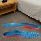 Par de palmilhas ortopédicas X, para pés chatos, planos, pisada pronada, posicionado sobre tapete cinza em cenário de quarto, destacando o revestimento superior em tecido azul texturizado com formato ergonômico para suporte plantar
